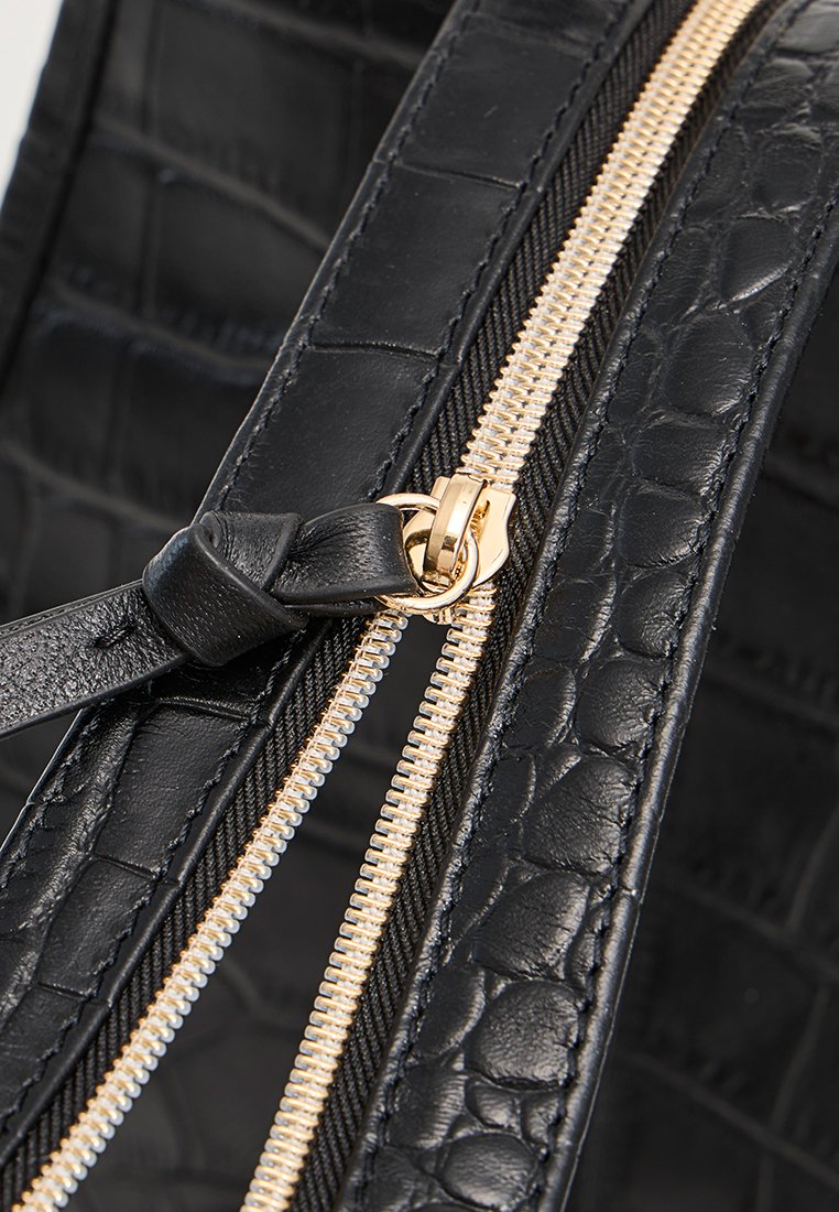 Borsa in pelle nera con texture a coccodrillo, con zip color oro e un bordo in tessuto nero. Vista ravvicinata della zip e dei dettagli delle parti metalliche.