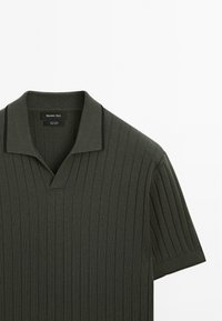 Dark green polo shirt made of cotton with vertical ribbing, short sleeves, and a V-neck. Features a contrasting black collar trim.