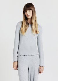 Haut à manches longues gris clair avec ourlet et poignets festonnés, réalisé en tissu doux. Le design présente un col rond classique et une coupe ajustée.