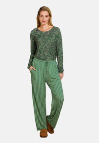 Groene bloemen top met lange mouwen gecombineerd met groene gestreepte wijde broek. De outfit heeft een ontspannen pasvorm en zijzakken. Bruine schoenen maken de look compleet.