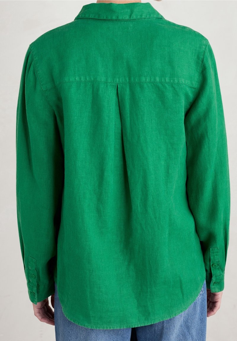 Vue de dos d'une personne portant une chemise à manches longues vert vif avec un pli au centre et un jean bleu.