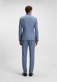 Jasnoniebieski garnitur o dopasowanym kroju, z klapami w kształcie notcha, pojedynczym rozcięciem i wąskimi spodniami. Gładki materiał z subtelnymi detalami teksturalnymi.