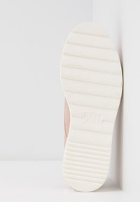 Baskets rose pâle avec semelle en caoutchouc blanc, arborant des rainures horizontales et un logo sur la semelle extérieure. Tige en textile lisse.