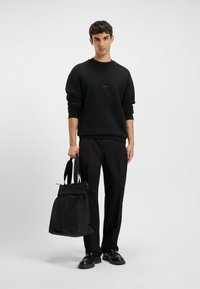 Felpa nera con logo verde, abbinata a pantaloni neri. Tiene una borsa a tracolla nera con manici e un dettaglio logo.