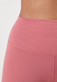 Mallas de talle alto en color rosa, hechas de un material suave y elástico, con una cinturilla plana y detalles de costura sutiles.