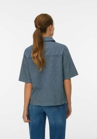 Camisa de manga corta en rayas navy y blancas, con cuello, corte relajado y detalle en el yugo trasero. Combinada con jeans de talle alto.