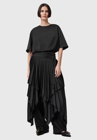 Sort outfit bestående af en løs kortærmet top og en lagdelt, plisseret nederdel med asymmetrisk kant. Fremstillet af glat stof med spænde detaljer.