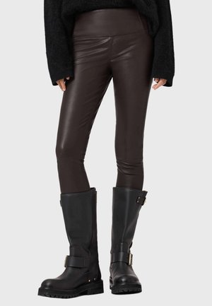 Leggings en simili cuir marron associés à des bottes noires montantes avec des boucles dorées et des semelles épaisses. La tenue a un design élégant et ajusté.