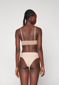 Bralette bege sem costuras com alças finas, combinada com parte de baixo de biquíni de cintura alta correspondente. Tecido suave, design minimalista, contornos subtis.