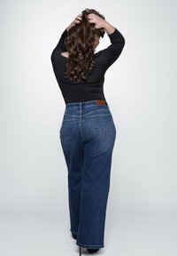 High-waisted denim jeans met een lichte wassing, brede pijpen en gestikte achterzakken. Zwarte top met lange mouwen gedragen, haar los gestyled.