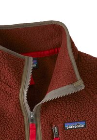 Giacca in fleece color ruggine con bordi grigi, colletto mezza zip e fodera rossa. Presenta una cerniera e un logo sul davanti. La texture è morbida e pelosa.