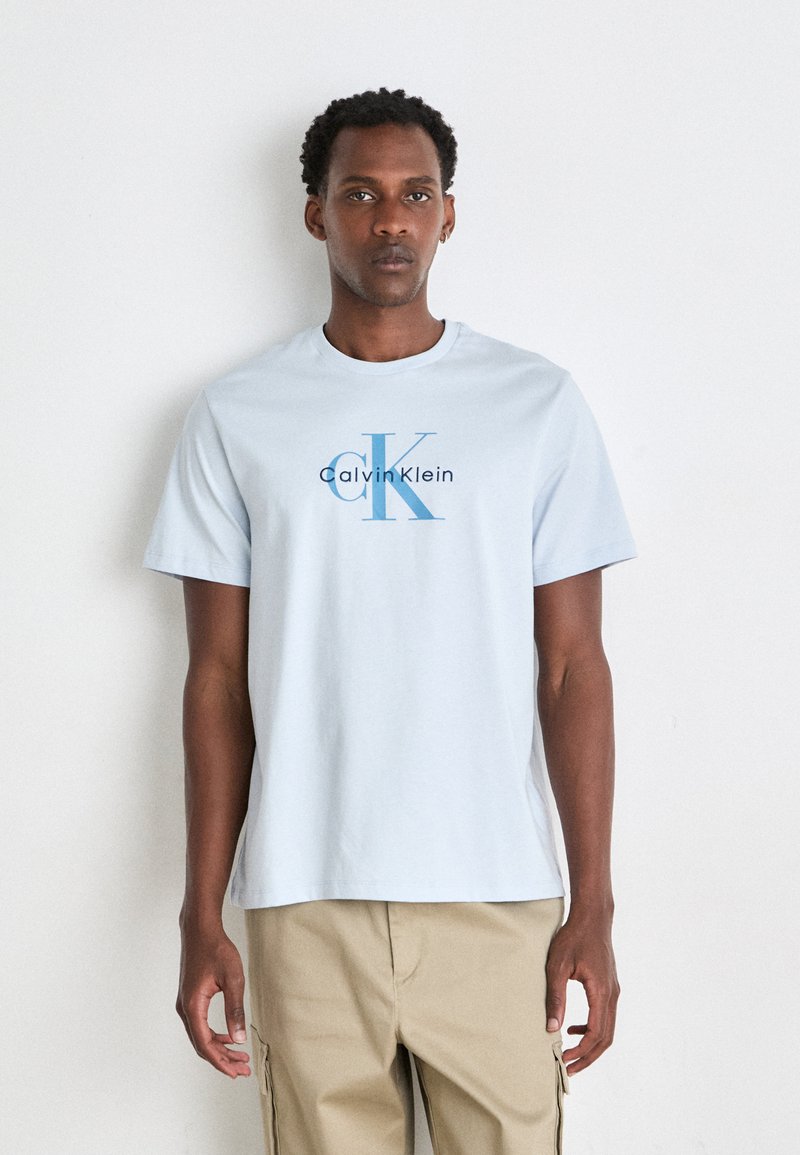Camiseta de algodón de color azul claro con cuello redondo y mangas cortas. Presenta un destacado logo de Calvin Klein en azul marino y azul en la parte frontal.