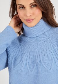 Pull en col roulé bleu clair avec des motifs texturés et des accents côtelés au col et aux manches. Fabriqué dans un matériau tricoté doux.