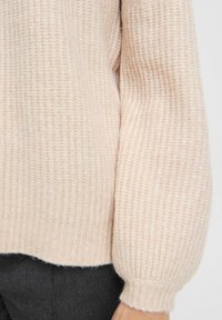 Waffelstrick-Pullover in Hellrosa mit geripptem Bündchen und Saum. Hat eine weiche Textur und einen lässigen Schnitt, teilweise am Arm gezeigt.