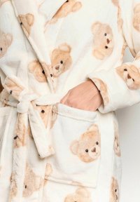 Biancheria da bagno in pile di colore crema con un motivo di facce di orsetti marroni chiari. Dotato di chiusura a cravatta e tasca laterale. Texture morbida.