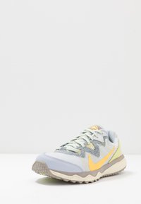 Scarpa da corsa grigia e gialla con una tomaia in mesh testurizzato, lacci a contrasto e una suola robusta. Presenta un distintivo logo Nike.