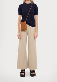 Námořnické tričko s krátkým rukávem, béžové široké kalhoty a černé sandály na platformě. Hnědá tkaná crossbody kabelka dodává texturu a detail.