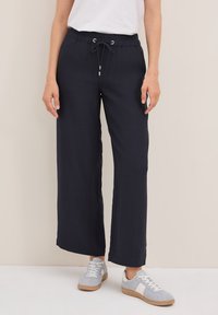 Navy blauwe wijde broek in een textuurstof met een elastische tailleband, verstelbaar trekkoord en zilveren oogjes, gecombineerd met grijze sneakers.