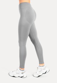 Leggings gris avec une taille haute et des motifs texturés, associés à des baskets de sport blanches et noires. Tissu lisse, coupe ajustée.