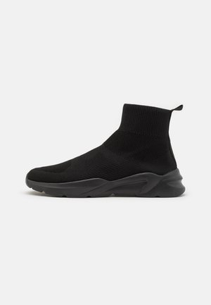 Sort højtop-sokkesneaker med tekstureret strikstof og tyk gummisål, vist fra siden på en ensfarvet hvid baggrund.