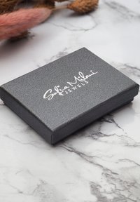 Svart texturerad smyckeslåda med en metallisk silverlogotyp som visar "Sofia Milani Jewels" på ovansidan. Enkel rektangulär form.
