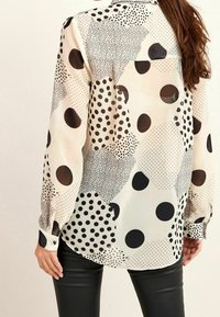 Long-sleeve blouse in lightweight, sheer fabric with an abstract pattern of dots in black and cream on a pale background. Buttoned cuffs.
