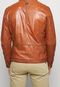 Brun läderjacka med en slät textur, som har söms detaljer och en synlig varumärkestagg, sedd bakifrån.