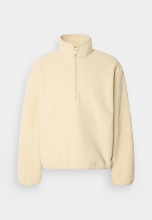 Beige fleece-pullover med hög krage och halvdragkedja. Har en mjuk textur och en löst sittande form.
