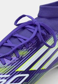 Ciorap de fotbal sintetic violet cu o guler de tip șosetă, șireturi plate și dungi diagonale îndrăznețe alb și verde lime pe lateral.