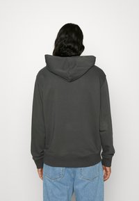 Sudadera con capucha de color gris oscuro, con una gran capucha, puños y dobladillo acanalados, y un corte relajado. Combinada con jeans desgastados de color azul claro.