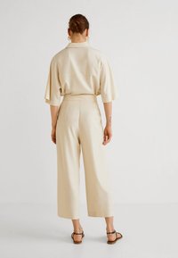 Beige, losvallend top met korte mouwen en een bijpassende hoge taille, wijde broek. Glad materiaal, minimalistisch ontwerp en sandalen met enkelbandjes.