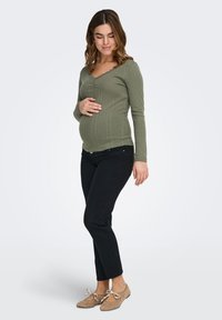 Olivzaļš ribots garroku tops ar viļņotu izgriezumu, kombinēts ar melnām džinsa biksēm un bēšām dzīvokļveida kurpēm ar loku akcentiem.