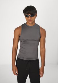 Haut sans manches gris en tissu extensible avec un col rond, associé à un pantalon noir à taille élastique avec cordon de serrage.