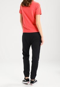 Růžové tričko s krátkým rukávem v kombinaci s černými úzkými tepláky; tepláky mají elastické manžety a kapsy, obuté s černými teniskami.