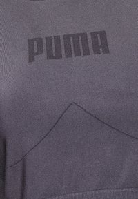 Violetti urheilu paita, jonka kankaassa on tekstuuria, mukana suuri musta "PUMA"-logo ja hienovarainen geometrinen muotoilu helman ympärillä.