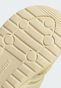 Cream-colored sneaker sole with textured rubber, featuring horizontal grooves and circular indentations. "adidas" is embossed on the side.