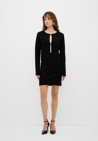 Schwarze strukturierte Jacke mit einem Schlüsselaugen-Frontdesign, kombiniert mit einem passenden, taillierten Rock. Beide Teile bestehen aus einem festen Stoff.