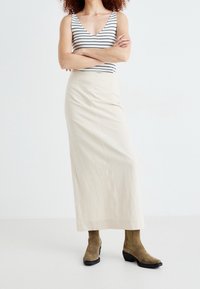 Top senza maniche a righe e gonna maxi crema. La modella indossa stivali alla caviglia in suede oliva. Tessuto morbido, vestibilità rilassata.