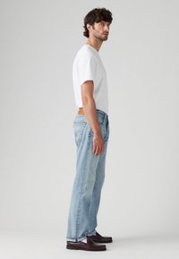 Witte katoenen t-shirt, lichtblauwe denim jeans, leren bruine riem en donkerbruine loafers. Rechte jeans met zichtbare stiksels.