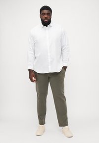 Chemise blanche à boutons associée à un pantalon vert olive et des baskets beiges, présentant une coupe droite et un col classique.