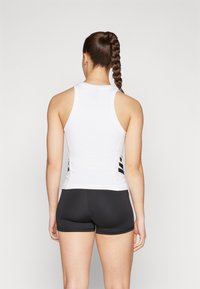 Λευκή αθλητική μπλούζα με σχέδιο racerback, με μαύρες πλαινές λεπτομέρειες. Συνδυασμένη με εφαρμοστά μαύρα σορτς, με λεία υφή υφάσματος.