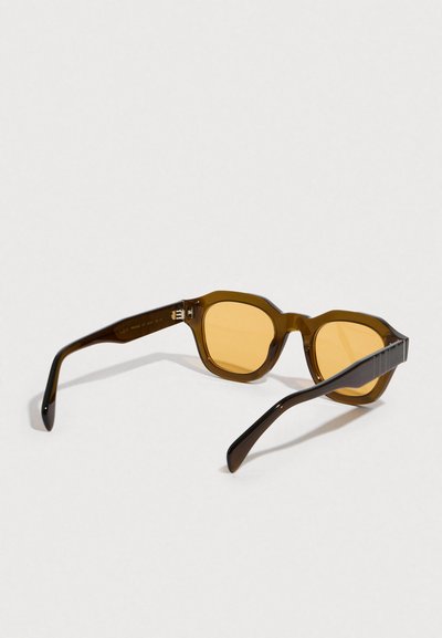 Gafas de sol de plástico marrón con lentes tintadas de amarillo, forma de montura octogonal y varillas elegantes y curvadas con un patrón texturizado.