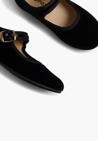 Černé sametové boty s kulatou špičkou a plochou podrážkou. Mají pásek se zlatým přezkou a elastický prvek kolem otvoru pro pohodlné nošení.