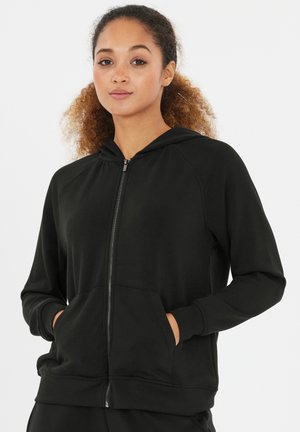 Haut à zip noir en tissu doux, avec capuche, poches avant et poignets et ourlet côtelés. Texture lisse avec une coupe décontractée.