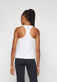 Top atletico bianco senza maniche con un retro rotondo, caratterizzato da una consistenza liscia e un piccolo logo "casall" sul collo, abbinato a leggings neri.