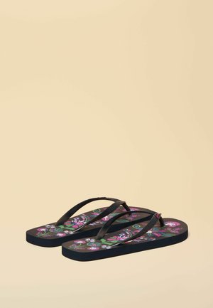 Paar schwarze Flip-Flops mit lila, grünen und weißen Blumenmustern auf der Fußsohle, dargestellt vor einem beigen Hintergrund.