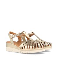 Sandalias metálicas doradas con diseño recortado, correa alrededor del tobillo, plantilla acolchada y suela blanca gruesa. Adecuadas para usar en clima cálido.