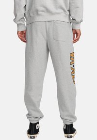 Pantaloni sportivi grigi con vestibilità rilassata, caratterizzati da una grande stampa grafica in arancione e nero sul lato e una sola tasca posteriore.