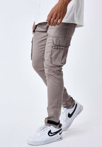 Pantalones cargo beige con bolsillos laterales, corte ajustado y una textura suave. Combinados con zapatillas blancas con detalles en negro.