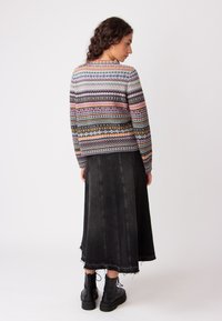 Maglione lavorato a maglia con motivi geometrici multicolori, sfondo grigio, abbinato a una lunga gonna di jeans nera con orlo sfilacciato e stivali neri chunky.